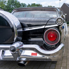 Round red lights, back of the black American classic car. Chrome bumper and spare tyre