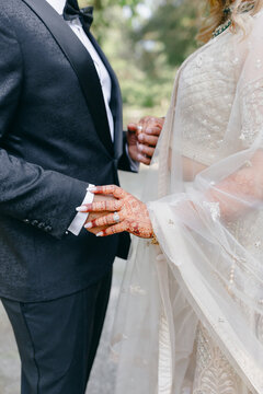 Indian bride's hands are decorated with traditional patterns and henna designs. The bride and groom hold hands close-up. Engagement ring with a large precious stone. Drawings on the hands of the bride
