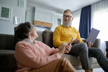 Obraz premium Smiling retired couple using digital gadget while resting at home