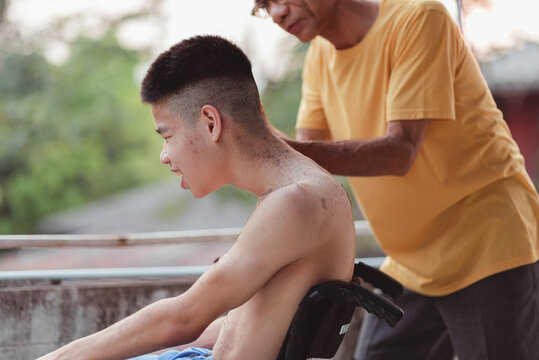 Young man with disability in wheelchair cutting hair by Hairdresser or parent, volunteer, caregiver, barber in the house or nursing home, personal hygiene care, health care and medical concept.