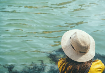 Back view of a elegant dressed woman wearing a hat and sitting on the waters edge in Venice.