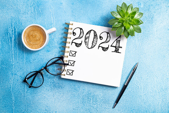 New year resolutions 2024 on desk. 2024 goals list with notebook, coffee cup, plant on blue table. New Year 2024 resolutions. Resolutions, plan, goals, action, checklist, idea concept. Copy space