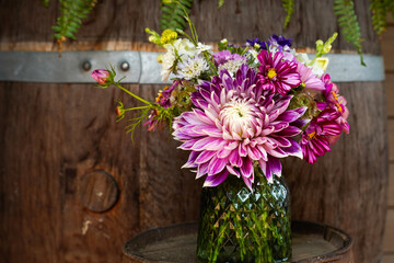 Bouquet of beautiful summer flowers in a green vase. Located in front of a large whiskey barrel. Focal flower is a large Vancouver Dahlia.