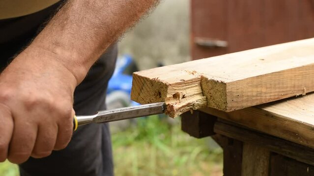 View of the hands of a worker who, with a chisel and a hammer, breaks off a piece from a board lying on a layout.