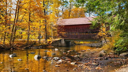 Red, wooden, covered bridge with beautiful autumn colors and river reflections, Stowe, Vermont, USA