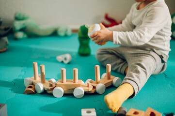 A toddler is holding a baby bottle with liquid and taking a break from playing with a montessori toy.
