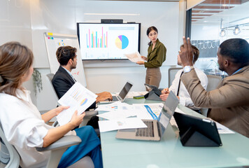 Asian woman present business work on monitor or screen and African American rest his hands to ask question in meeting room with multi-ethnic coworkers.