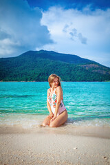 Young woman in a bikini enjoys a sunny day on the beautiful tropical beach. Concept of summer vacation and relaxation.