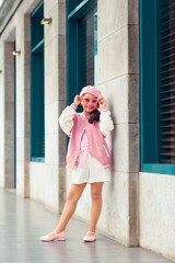 Retrato de linda niña sonriente con atuendo rosa y gafas de sol rosa en la ciudad