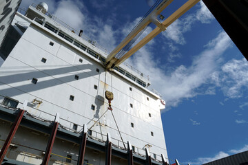White superstructure with navigational bridge on the merchant container ship with cranes and hooks observed from main deck during sunny day with blue sky with clouds. There are visible cell guides. © Lucia