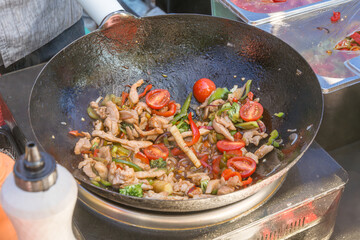 Cooking Asian food from meat, seafood and vegetables in a wok on the street. Fast food