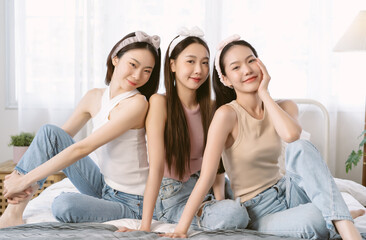 Group of Asian Girl friends feeling happy posing together sitting on bed. Smiling korean blogger influencer girls skincare, wellness makeup routine, look at camera at home. Friendship concept