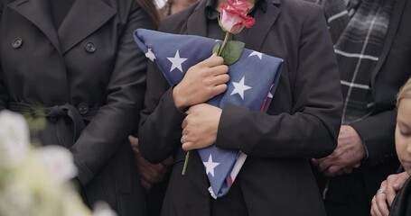 Funeral, graveyard and woman with American flag for veteran for respect, ceremony and memorial service. Family, depression and sad people with flower in cemetery for military, army and soldier hero