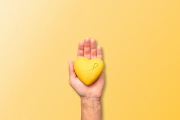 A hand holding a yellow resin heart adorned with a yellow bow, symbolizing 'Yellow September',...