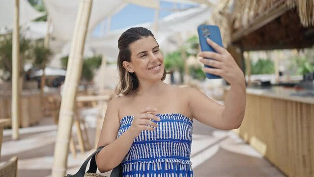 Young hispanic woman taking a selfie picture standing at sunny restaurant terrace