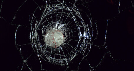 Ball of Baseball breaking Pane of Glass against Black Background