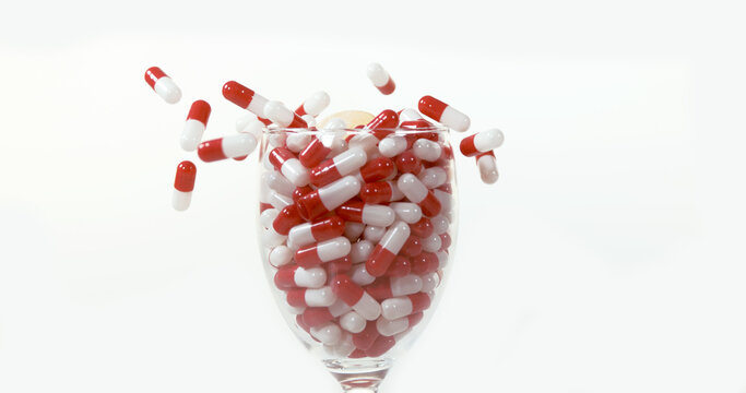 Capsules Falling into a Glass against White Background