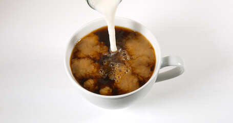 Milk poured into a Cup of Coffee against White Background