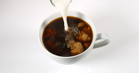Milk poured into a Cup of Coffee against White Background