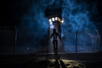 Obraz premium Old prison watchtower protected by wire of prison fence at night. Creative art decoration. Selective focus