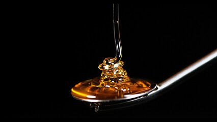 Honey Flowing on Spoon against Black Background