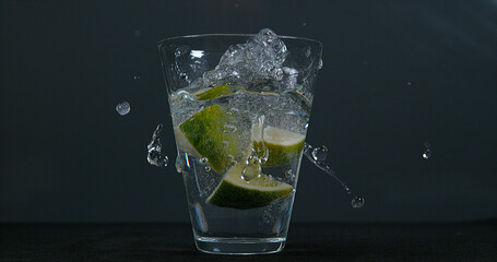 Green Citrus, citrus aurantifolia, falling into a Glass of Water,