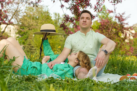 young married couple enjoying picnic city park, captured in close-up with voyeuristic effect through apple tree leaves. concept of savoring life, strong relationships, mental well being, prosperity