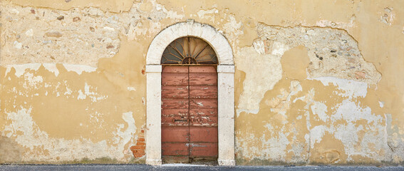 Rustic crumbling house wall with beautiful old door in Tuscany.