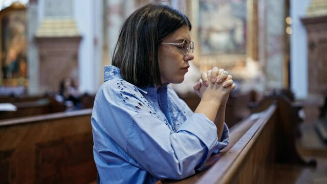 Young beautiful hispanic woman praying on a church bench at St. Karl Borrom&auml;us church