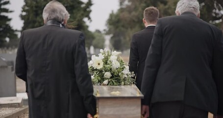 Men, coffin and pallbearers walking at cemetery ceremony outdoor at burial tomb. Death, grief and group casket at funeral, carry to graveyard and family service of people mourning at windy event.