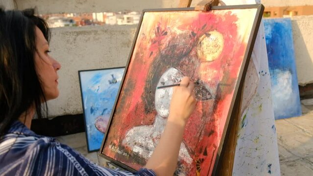 A Woman artist paints a painting on the rooftop of a building outdoors on sunny day