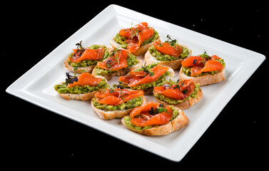 Bruschetta with salmon, avocado and microgreens in a white plate.