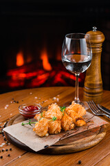 Fried chicken nuggets with spices, ketchup and a glass of water on a background of a fireplace.