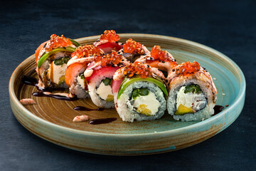 Sushi rolls with tuna, salmon, eel, cream cheese, avocado, red caviar and sauce in plate.