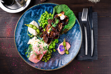 Asian breakfast beef slices with cabbage, beans, egg and microgreens on wooden table.