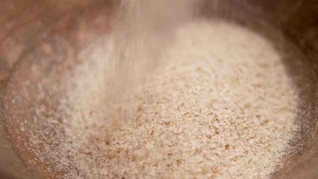 Superfood psyllium husk filling a wooden bowl closeup in slow motion. Prebiotic for Digestive Microflora and Detox