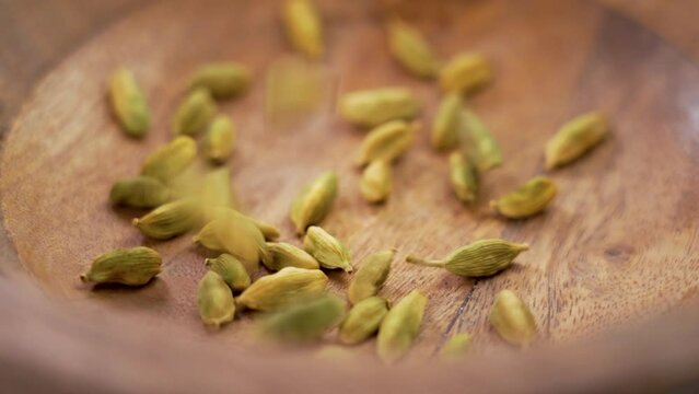 Dried cardamon seed pods falling into a wooden kitchen bowl. Green natural spicy herb cardamom seasoning. Slow motion. Macro shot. Rotation