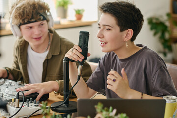 Cute teenage girl sing in microphone during broadcast from home while sitting in front of camera...