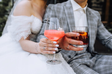 The bride and groom hold glass glasses with an alcoholic cocktail in their hands, whiskey in their hands at a party. Wedding photography, portrait.