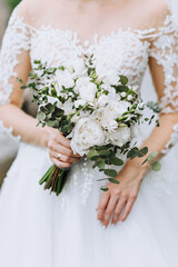 The bride in her hands holds a bouquet with white flowers of roses, peonies. Wedding photography, close-up portrait.