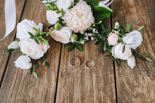 A bouquet of flowers, a boutonniere, golden rings of the newlyweds lie on a wooden background. Wedding photography closeup, top view, concept.