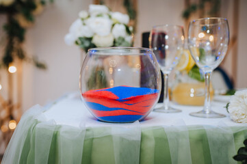 A glass bowl with colored, multi-colored kinetic sand, a bouquet of flowers is on the table. Close-up wedding photography, decor, design.