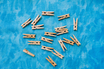 A lot of small wooden clothespins lying on a blue fabric background. Photography, household, background.