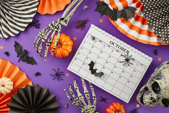 It's time to get set for Halloween. Top view photo of calendar, halloween decorations, paper props, skull, skeleton hands, pumpkins on purple background