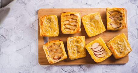 Small upside-down puff pastry cakes with banana and apple on a board top view web banner