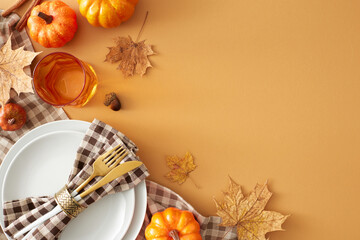 Vibrant autumn table arrangement. Top view photo of plate, cutlery, checkered tablecloth, cinnamon sticks, pumpkins, autumn leaves, glass on pastel brown background with ad slot