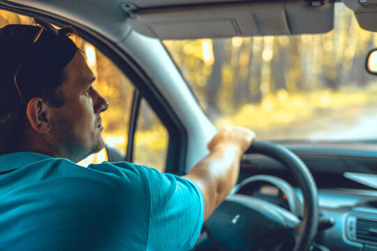 Portrait. Handsome Man Driving A Car Looks In The Rearview Mirror While Traveling. A Nice Man Is Traveling In His Car Around The Country. Concept Of A Male Traveler Driving A Car.