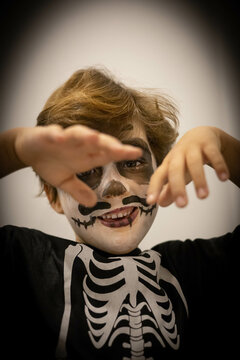 Young 7 years old kid in a costume of Mexican día de los muertos  skeleton and skull, smiling and looking at camera, ready for Halloween for the school party.