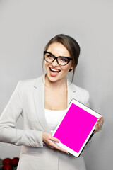 Beautiful young woman wearing jacket and black-framed glasses has excited facial expression while demonstrating something on digital tablet. Empty pink screen for custom design. Product advertising.