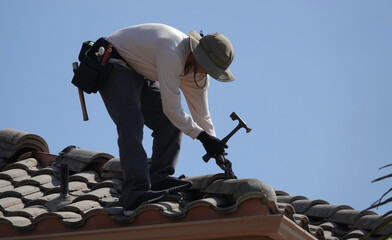 Silhouette of a roofer using a hammer to pry off roof tile   